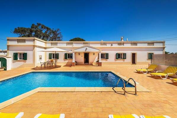A two-story house with a swimming pool, outdoor seating, and a covered patio area.