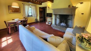 A cozy living room with a fireplace, wooden beams, a sofa, and a dining area. - Cottage, private pool, beautiful mountain views, WIFI. (nicciano)