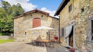 A stone building with a patio area featuring a table and chairs, a lounge chair, and a potted plant. - Cottage, private pool, beautiful mountain views, WIFI. (nicciano)