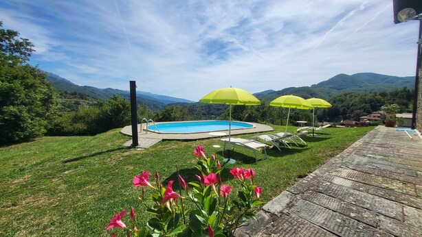 A backyard with a swimming pool, green umbrellas, and a view of mountains. - Cottage, private pool, beautiful mountain views, WIFI. (nicciano)