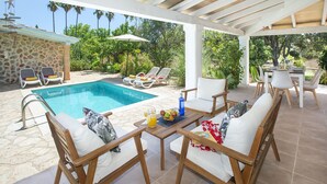 A covered outdoor area with a pool, lounge chairs, and a dining table set up for an outdoor meal. - VILLA ALMADRAVA - VACATION PARADISE (Pollensa)
