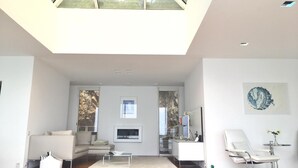 A spacious living room with a high ceiling, a sofa, a coffee table, and a dining area with a chair and table. - Spectacular Panoramic Views of Cap Ferrat & Beaulieu. (Villefranche-Sur-Mer)