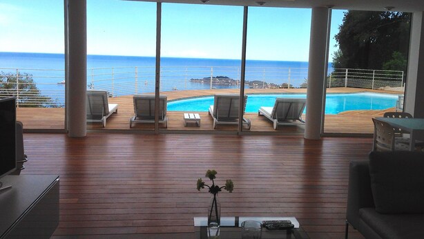 A spacious balcony with a pool, lounge chairs, and a view of the sea. - Spectacular Panoramic Views of Cap Ferrat & Beaulieu. (Villefranche-Sur-Mer)