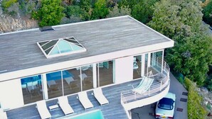 A modern house with a large glass balcony, a swimming pool, and a car parked nearby. - Spectacular Panoramic Views of Cap Ferrat & Beaulieu. (Villefranche-Sur-Mer)