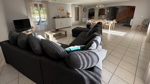 Un soggiorno moderno con un divano scuro, una TV a schermo piatto e un'area pranzo con sedie e tavolo in legno.