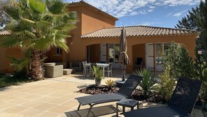 Una casa con patio piastrellato, mobili da esterno e una palma.