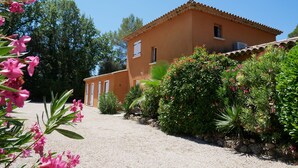 Un edificio a due piani con tetto in tegole, circondato da una rigogliosa vegetazione e piante fiorite.