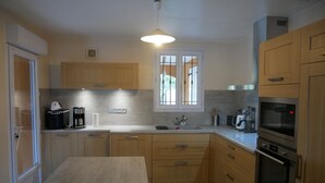 Una cucina moderna con mobili in legno, forno integrato, microonde e una finestra con inferriate.