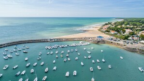 Ein Yachthafen mit vielen angestuften Booten, ein Sandstrand und eine Küstenstadt im Hintergrund.
