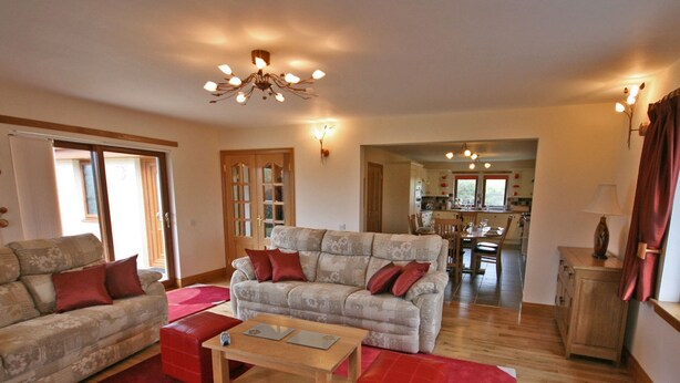A living room with a sofa, a coffee table, and a red ottoman. There is a wooden cabinet and a lamp on a side table.