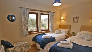A bedroom with two beds, a window with curtains, a bedside lamp, and a small table with a plant.