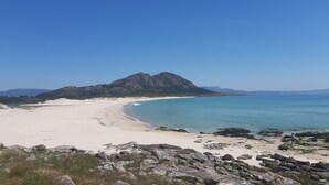 A beach with a rocky foreground, a sandy shore, and a mountain in the background. - Anchor House floor in Walls with wifi (Muros, A Coruña)
