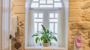 A bathroom with a stone wall, a wooden bench with towels, a potted plant, and a window with a view. - Anchor House floor in Walls with wifi (Muros, A Coruña)