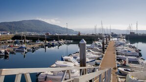 A marina with boats docked along a wooden pier, a clear sky, and a mountain in the background. - Anchor House floor in Walls with wifi (Muros, A Coruña)