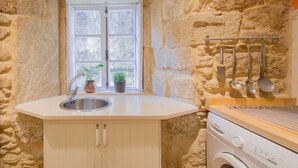 A kitchen with a stone wall, a window with a plant, a sink, and a washing machine. - Anchor House floor in Walls with wifi (Muros, A Coruña)