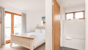 A bedroom with a bed, a bathroom with a bathtub, and a view of the outdoors. - Combermere Cottage - Two Bedroom Cottage, Sleeps 4 (Bude)