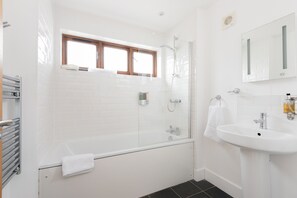 A modern bathroom with a glass-enclosed shower, a white sink, and a window above the bathtub. - Combermere Cottage - Two Bedroom Cottage, Sleeps 4 (Bude)