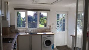 A modern kitchen with a built-in washing machine, large windows, and a view of the garden. - Well Equipped Family Holiday Home With Garden In A Quiet rural location. (Sutton)