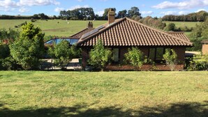 A rustic building with a tiled roof, surrounded by a grassy field and trees. - Well Equipped Family Holiday Home With Garden In A Quiet rural location. (Sutton)