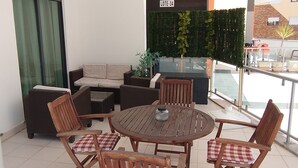 Un patio con una mesa redonda de madera, cuatro sillas de madera con cojines a cuadros, un sofá y una pequeña planta en maceta.