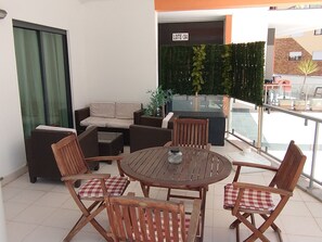 Eine Terrasse mit einem runden Holztisch, vier Holzstühlen mit karierten Kissen, einer Couch und einem kleinen Blumentopf.