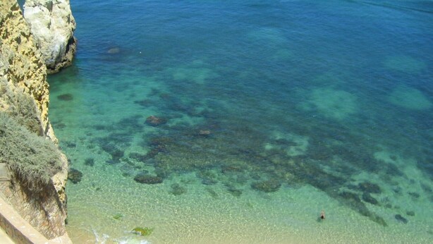 Una playa costera con agua cristalina, acantilados rocosos y una orilla arenosa.