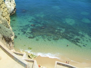 A coastal beach with clear water, rocky cliffs, and a sandy shore.