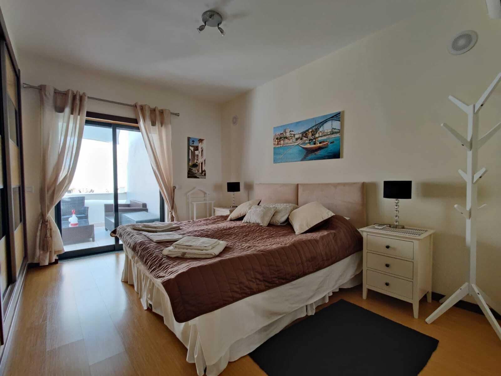 Une chambre à coucher avec un lit, des tables de chevet, un bureau et une vue sur l’extérieur.