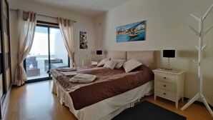 Un dormitorio con cama, mesitas de noche, un escritorio y vistas al exterior.