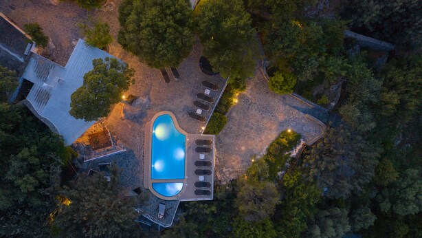 Vista aèria d'un complex turístic amb una piscina, gandules i un camí de pedra.