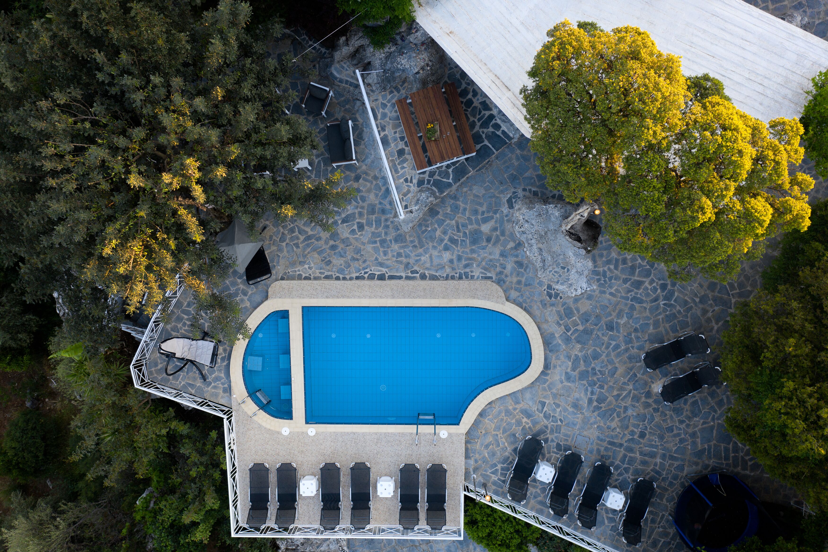 An aerial view of a swimming pool area with lounge chairs, a wooden deck, and a stone pathway.