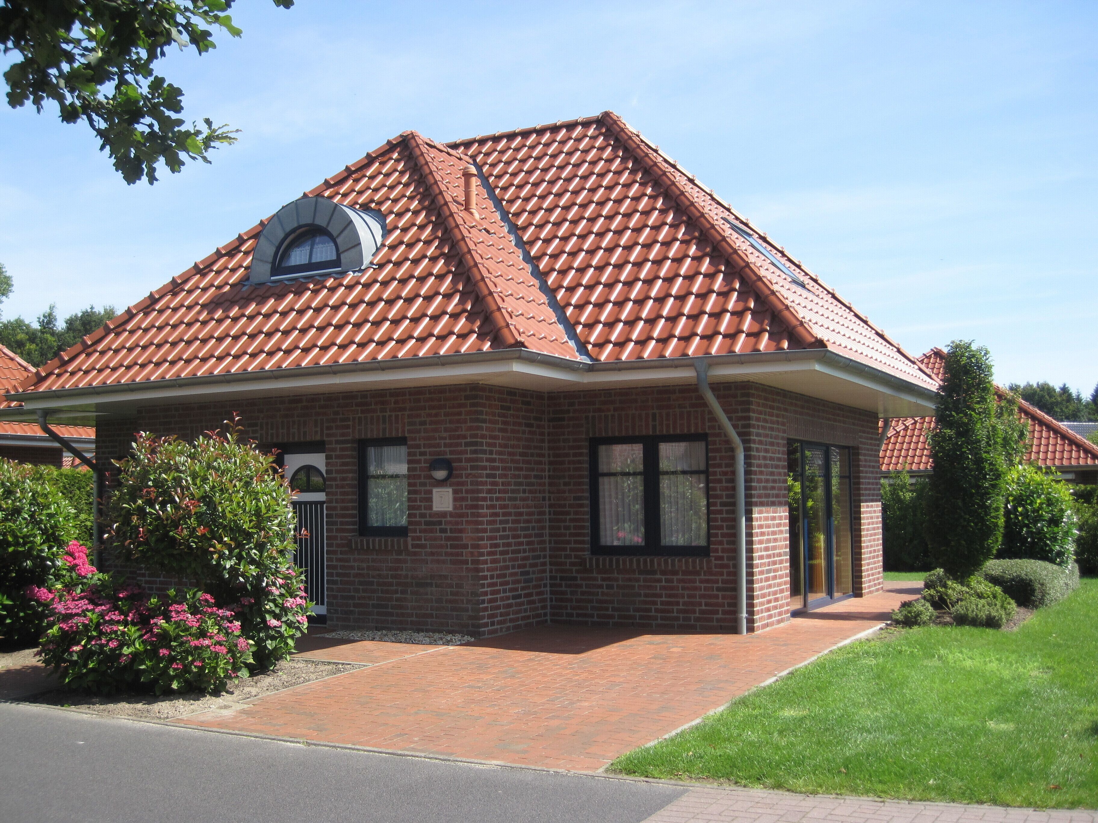 Et toetagers hus med røde tegltage, murstensfacade og en lille veranda.