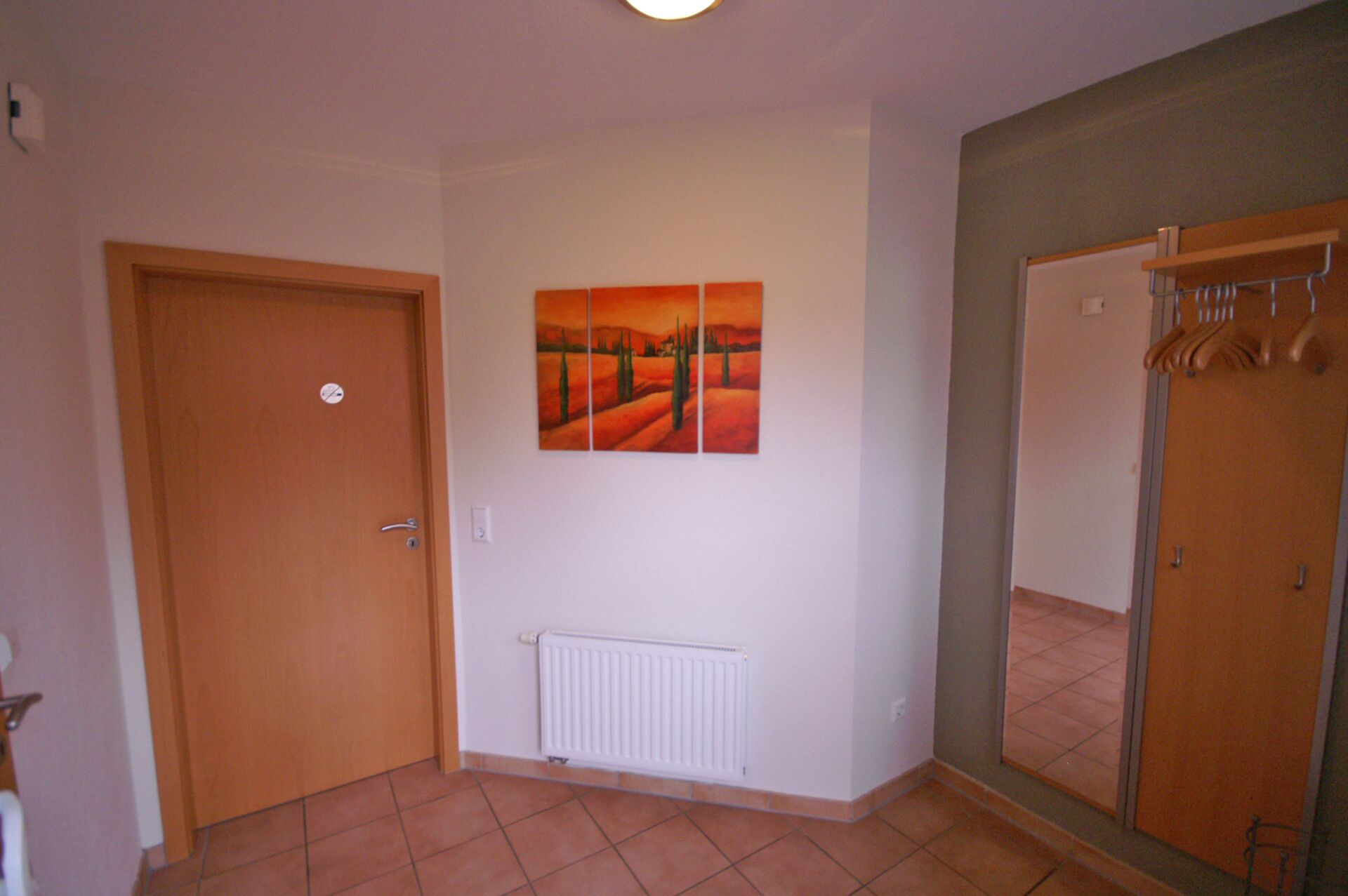 A hotel room with a door, a radiator, a painting, and a mirror.
