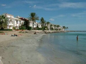 A beachfront property with a row of white buildings, palm trees, and a clear blue sky. - Terraced house for 8 by the beach in Aldeas de Taray Club, La Manga (San Javier)