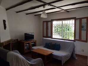 A living room with a sofa, a television, and a wooden cabinet. - Terraced house for 8 by the beach in Aldeas de Taray Club, La Manga (San Javier)
