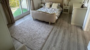 Un dormitorio con una cama grande, una mesita de noche con lámparas, un armario pequeño y vistas al exterior con vegetación.