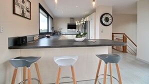 Una cocina moderna con una isla central, taburetes de bar, iluminación colgante y un reloj en la pared.