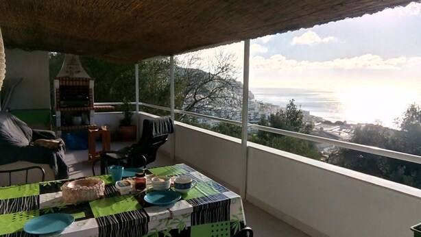 A balcony with a table set for dining, overlooking a coastal cityscape. - Rustic house, sea view, 6 people, terrace with barbecue.  (Sesimbra)