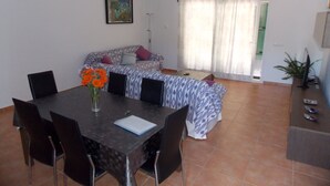 A dining area with a table, chairs, and a vase of flowers. There is a sofa with patterned cushions in the background. - New Villa With Private  Pool At Walking Distance From The Centre/Beach (Santanyí)