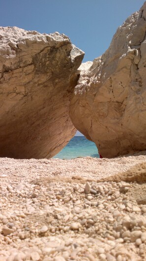Una spiaggia rocciosa con una formazione naturale che crea un'apertura a forma di tunnel verso il mare.