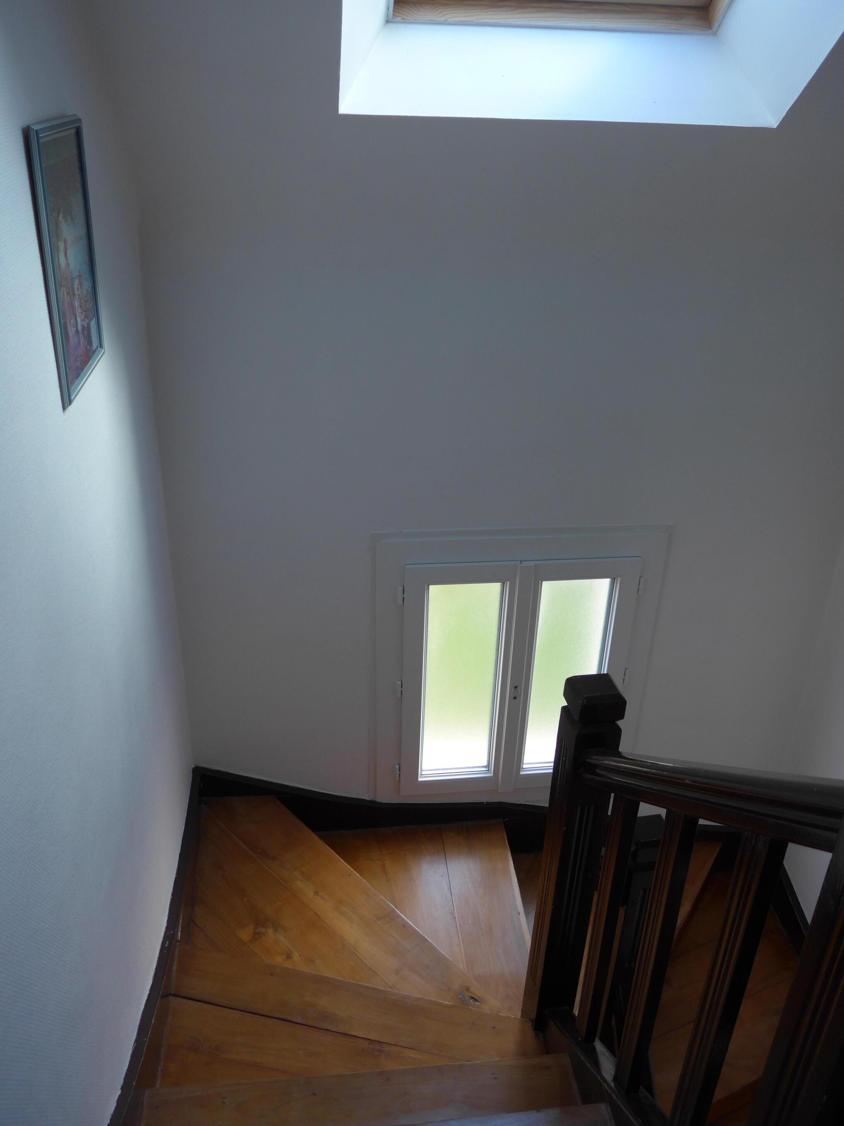 A staircase with wooden steps leading to a landing. There is a skylight above the landing, and a door with frosted glass panels.