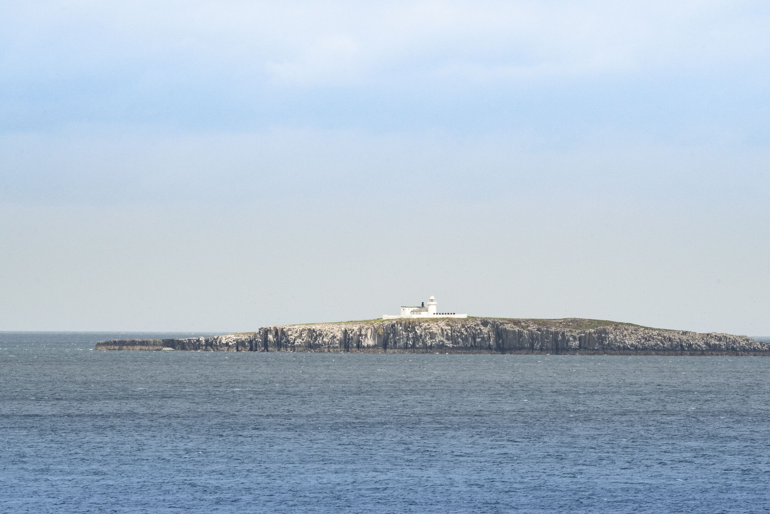 A lighthouse on a rocky island with a clear view of the surrounding water.