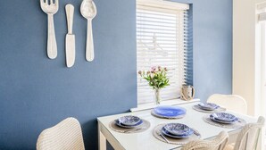 A dining area with a table set for four, a window with blinds, and a wall-mounted utensil holder. - Northern Hideaways Seascape (Seahouses)