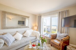Un salon comprenant un canapé, un fauteuil et une table basse, une télévision, ainsi qu’un balcon aménagé avec du mobilier d’extérieur.