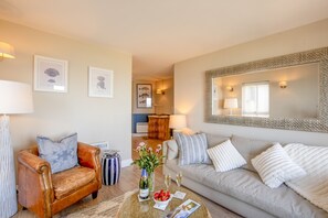 Un salon comprenant un fauteuil en cuir, un canapé, une table basse avec une bouteille et des verres, et des œuvres d’art encadrées accrochées aux murs.