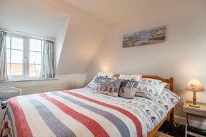 A bedroom with a bed, a window with curtains, a lamp, and a painting on the wall.