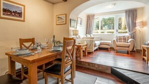 Un coin repas avec une table en bois dressée pour quatre personnes, un canapé et une fenêtre avec des rideaux.