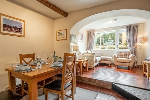 A dining area with a wooden table set for four, a sofa, and a window with curtains.