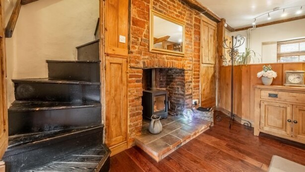 Un escalier mène à une pièce dotée d’une cheminée en briques, de murs en bois et d’une petite armoire contenant une horloge.