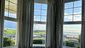 A room with three windows, each with a view of a coastal landscape, including buildings and greenery.